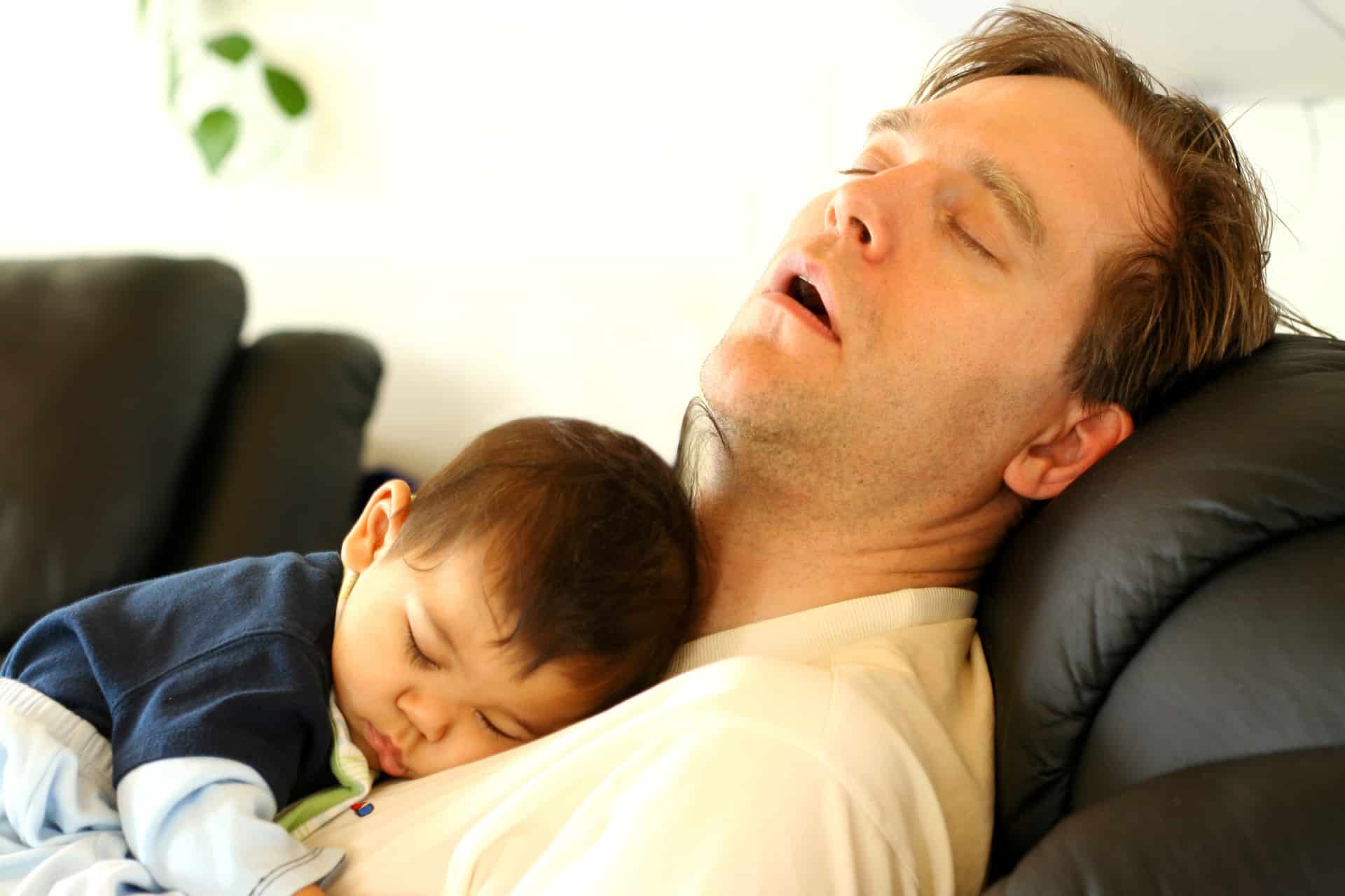 Father sleeping on chair with his baby boy on chest